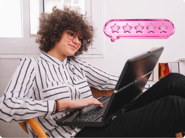 Mulher olha sorridente para o notebook que está no seu colo, ao seu lado existe o desenho de um balão em rosa com 5 estrelas.