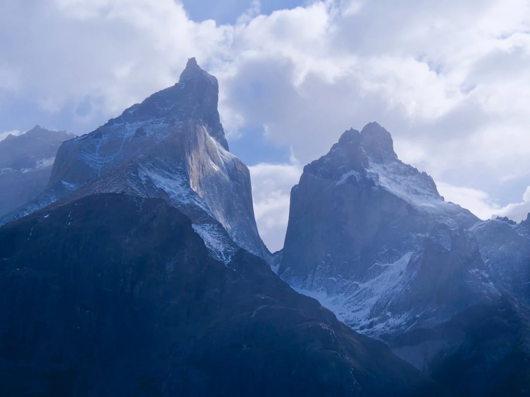 Montanhas de Torres del Paine, Chile, com picos nevados e nuvens altas ao fundo em dia claro. Monte seu roteiro com pontos Livelo.