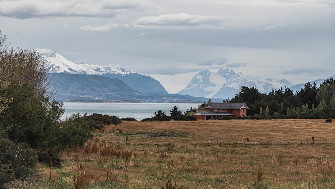 Paisagem rural na Patagônia chilena com casa ao longe, campo aberto e montanhas nevadas ao fundo. Organize com pontos Livelo.