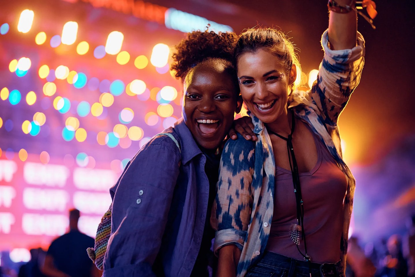 Duas amigas sorrindo em show noturno em Chicago, com luzes coloridas desfocadas ao fundo e clima de festival. Curta Chicago com pontos Livelo.