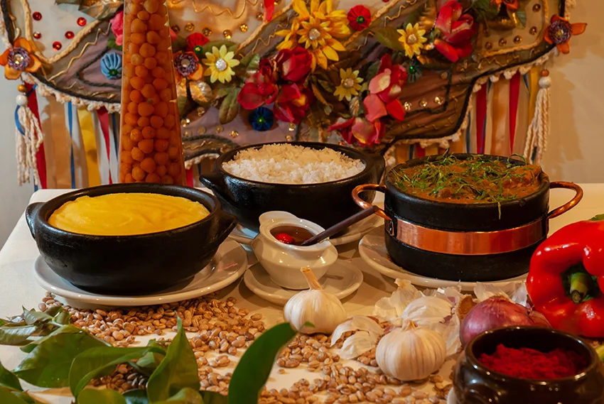 Mesa com comida típica mineira, panelas de barro, arroz e ingredientes regionais em destaque. Planeje sua viagem com pontos Livelo.