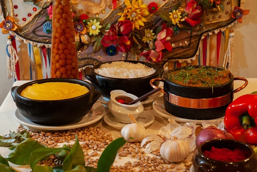 Mesa com comida típica mineira, panelas de barro, arroz e ingredientes regionais em destaque. Planeje sua viagem com pontos Livelo.