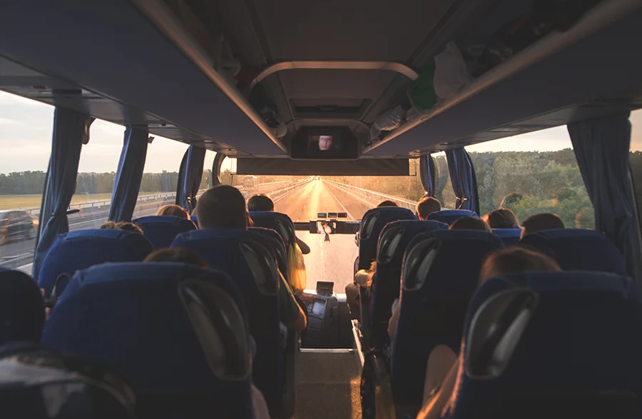 Interior de ônibus em estrada ao entardecer, passageiros sentados e luz dourada entrando pelas janelas. Planeje sua viagem com pontos Livelo.