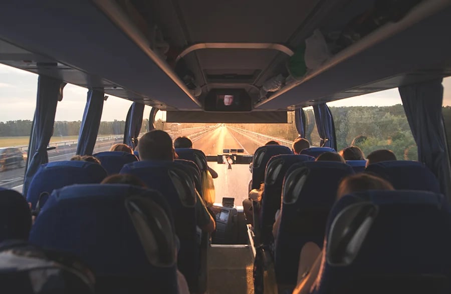 Interior de ônibus em estrada ao entardecer, passageiros sentados e luz dourada entrando pelas janelas. Planeje sua viagem com pontos Livelo.