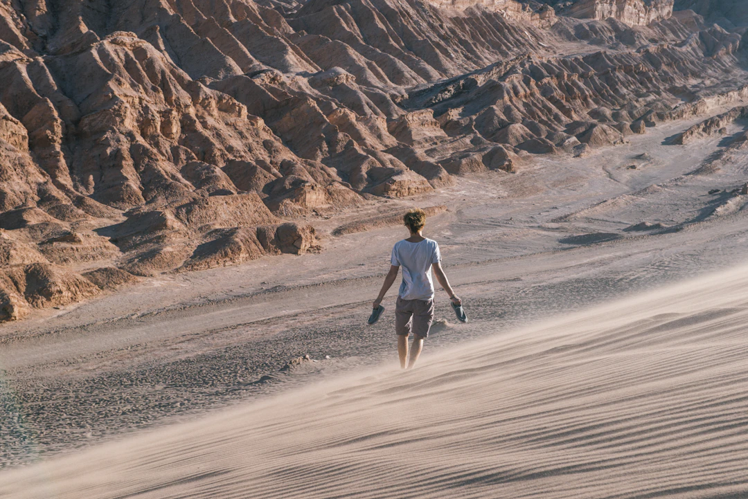 Pessoa caminhando nas dunas do Atacama com montanhas ao fundo. Viaje com pontos na Livelo.
