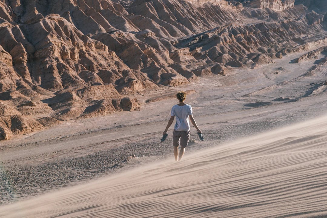 Pessoa caminhando nas dunas do Atacama com montanhas ao fundo. Viaje com pontos na Livelo.