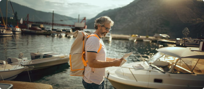 Homem com mochila nas costas sorri ao olhar um mapa em um píer.