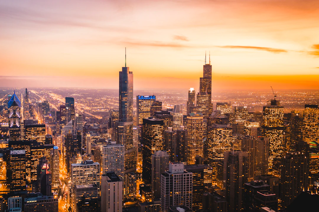 Vista panorâmica de Chicago ao anoitecer, com prédios iluminados e céu alaranjado sobre a cidade. Organize sua viagem com pontos Livelo.