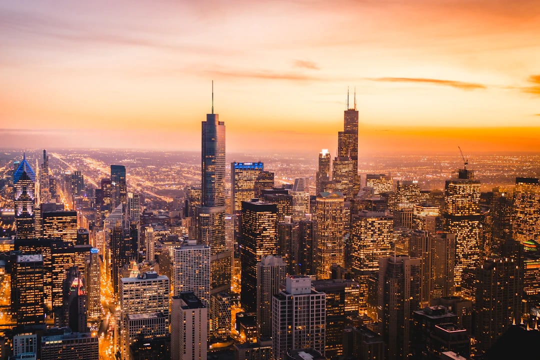 Vista panorâmica de Chicago ao anoitecer, com prédios iluminados e céu alaranjado sobre a cidade. Organize sua viagem com pontos Livelo.