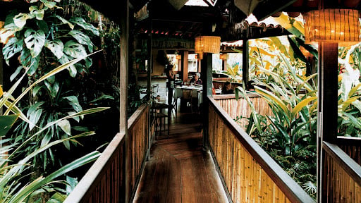 Salão do restaurante Manacá, luz baixa e clima aconchegante na mata. Descubra São Sebastião e planeje com pontos na Livelo.