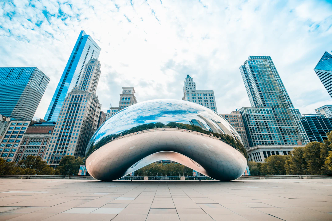 Escultura Cloud Gate, o The Bean, em Chicago, cercada por arranha-céus e praça vazia em primeiro plano. Inclua Chicago no roteiro com pontos Livelo.