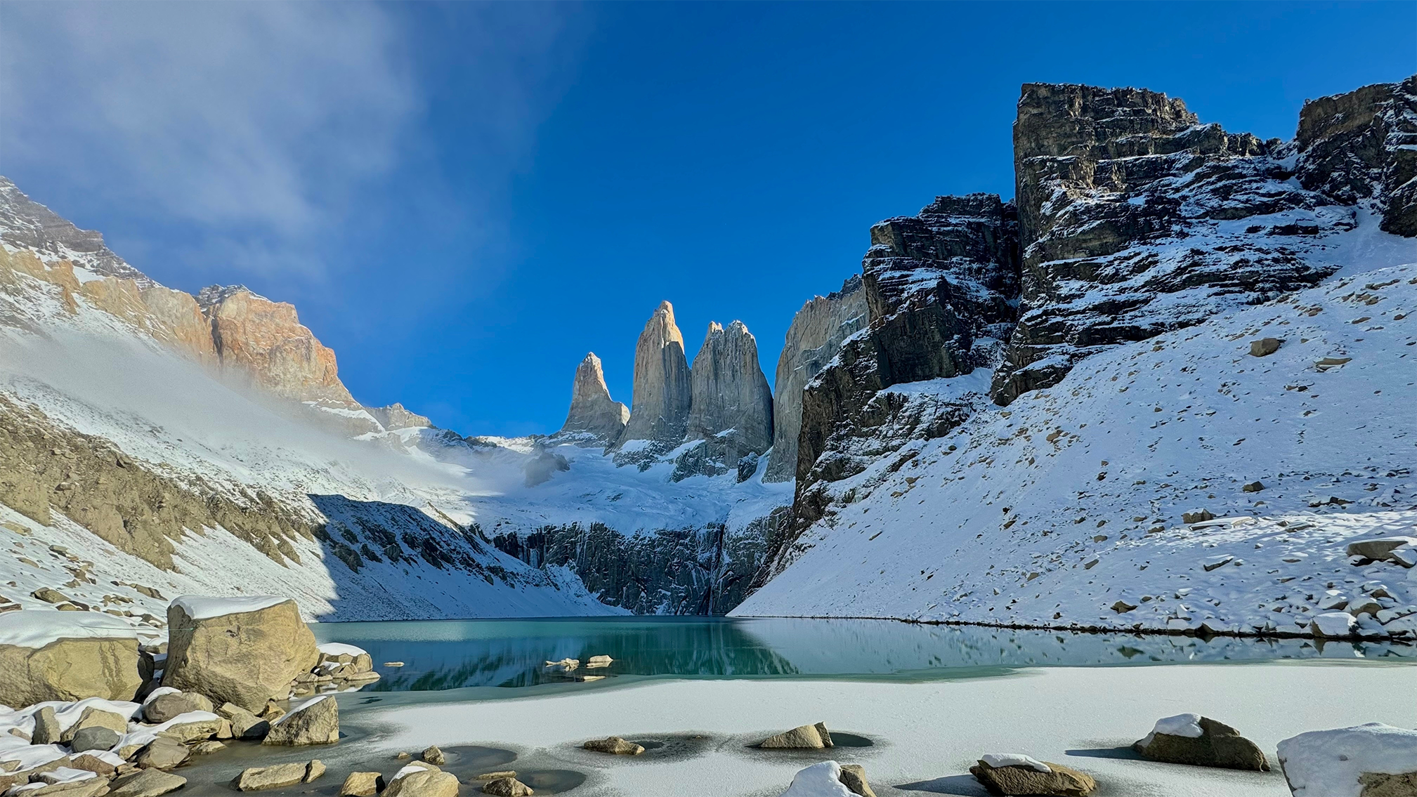 Lago glacial em Torres del Paine, Chile, com montanhas nevadas e as torres ao fundo sob céu azul. Planeje a viagem com pontos Livelo.