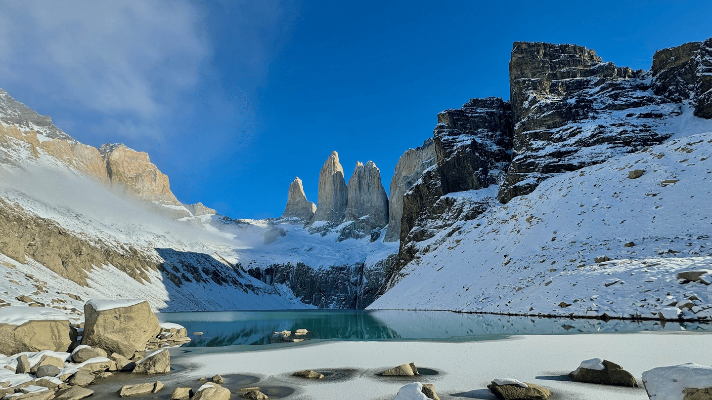 Lago glacial em Torres del Paine, Chile, com montanhas nevadas e as torres ao fundo sob céu azul. Planeje a viagem com pontos Livelo.