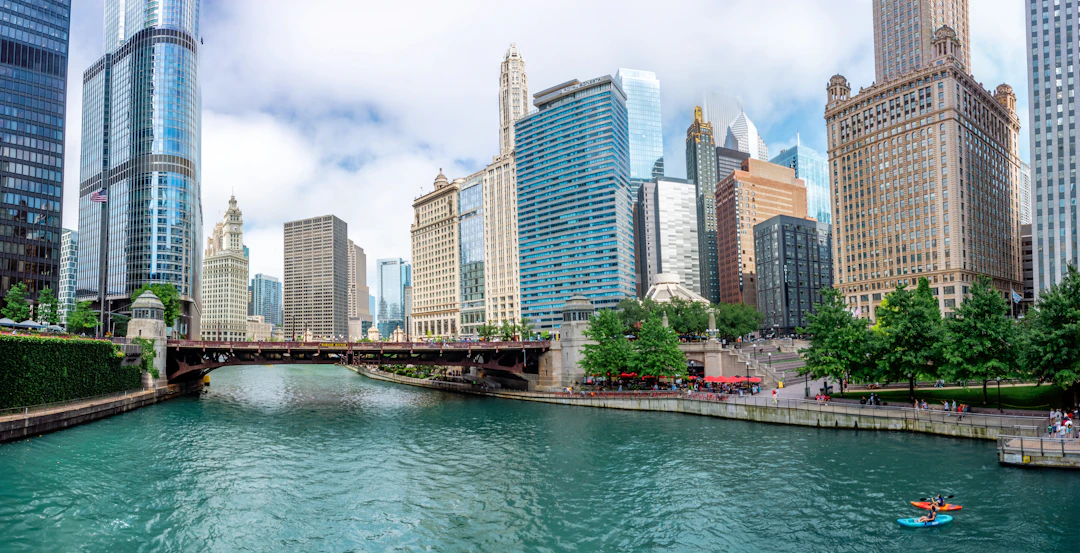 Vista do rio Chicago entre arranha-céus no centro da cidade, com edifícios modernos, ponte e caiaque na água. Explore Chicago com pontos Livelo.