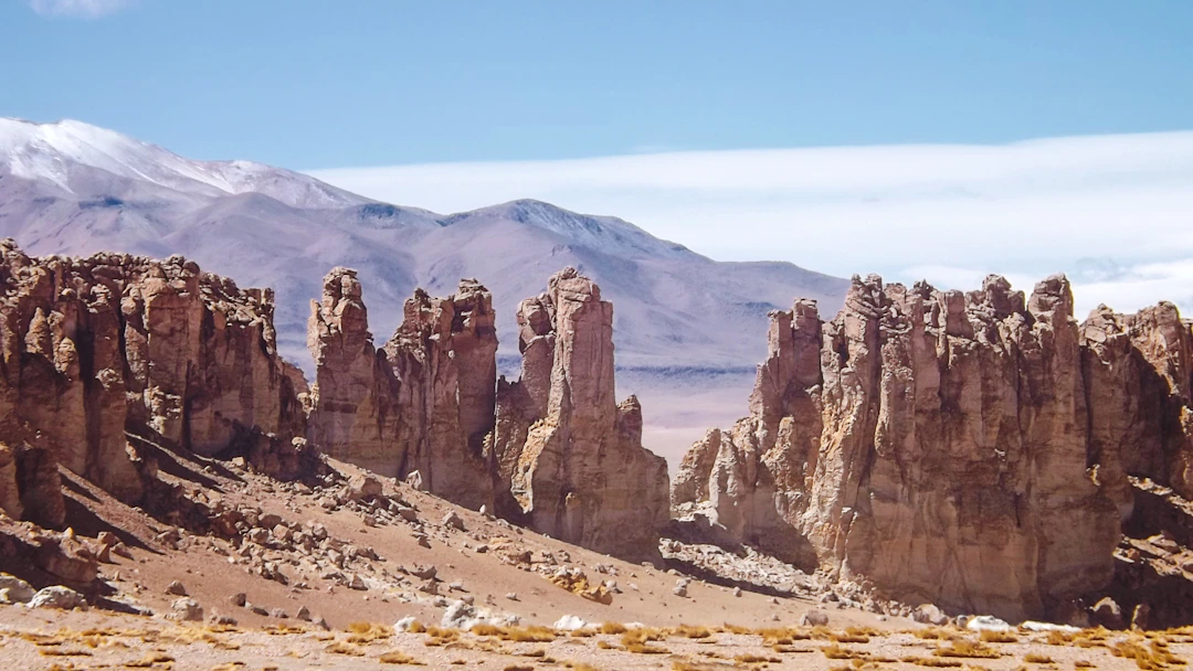 Formações rochosas no Atacama com montanhas ao fundo e luz intensa do deserto. Programe com pontos na Livelo.