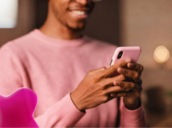 Uma pessoa sorridente, com blusão rosa, usando um celular