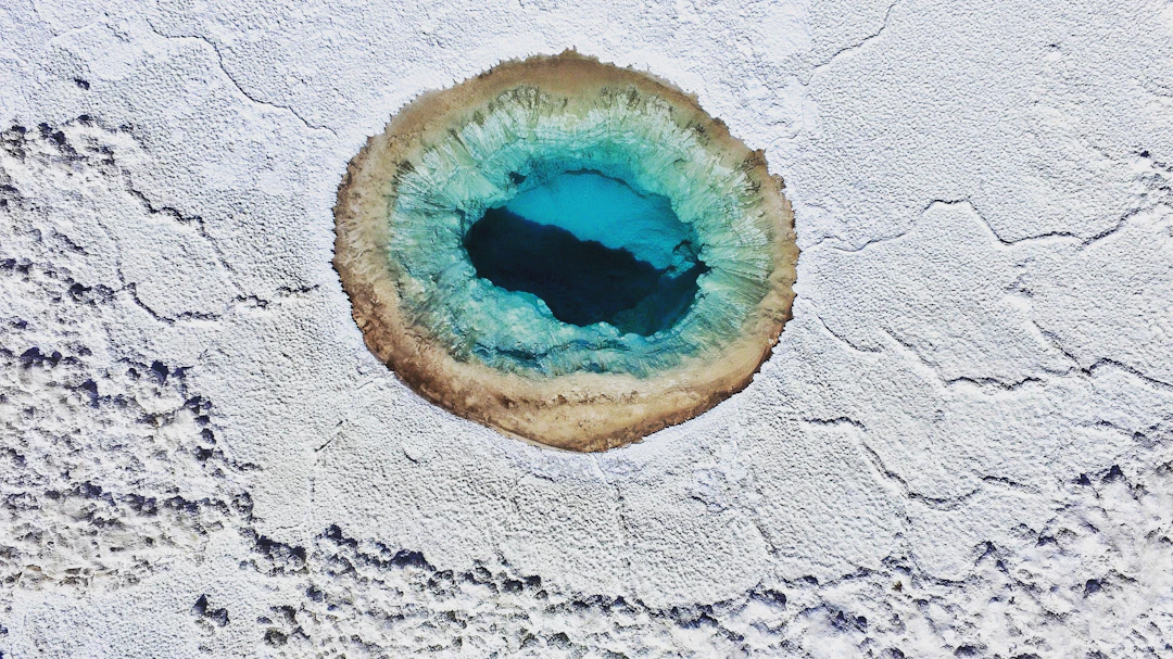 Vista aérea de lagoa azul em salar do Atacama, contraste forte com o branco do sal. Planeje com pontos na Livelo.