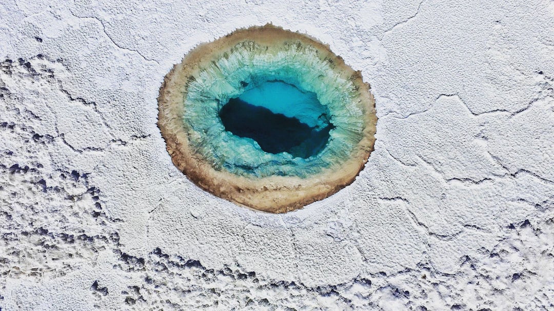 Vista aérea de lagoa azul em salar do Atacama, contraste forte com o branco do sal. Planeje com pontos na Livelo.
