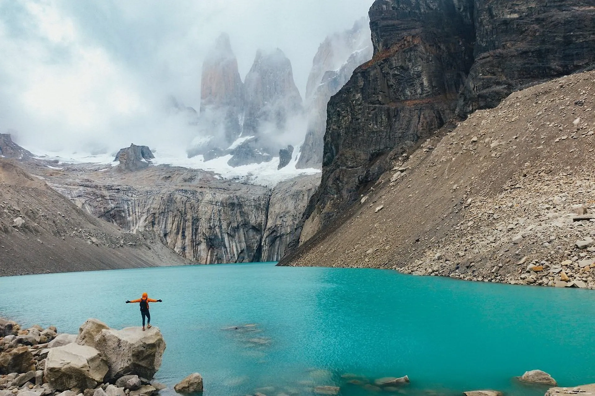 Paisagem de Torres del Paine, Chile, com lago turquesa, montanhas ao fundo e pessoa sobre rocha. Organize com pontos Livelo.