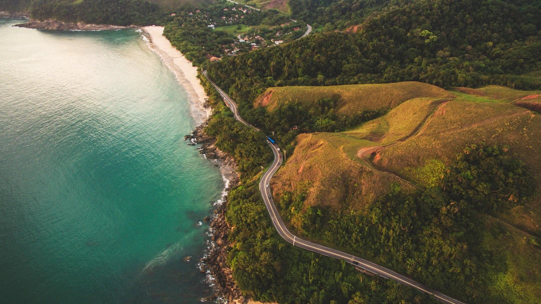 Vista da costa de São Sebastião com morros verdes e faixa de areia tranquila. Viaje com pontos na Livelo.