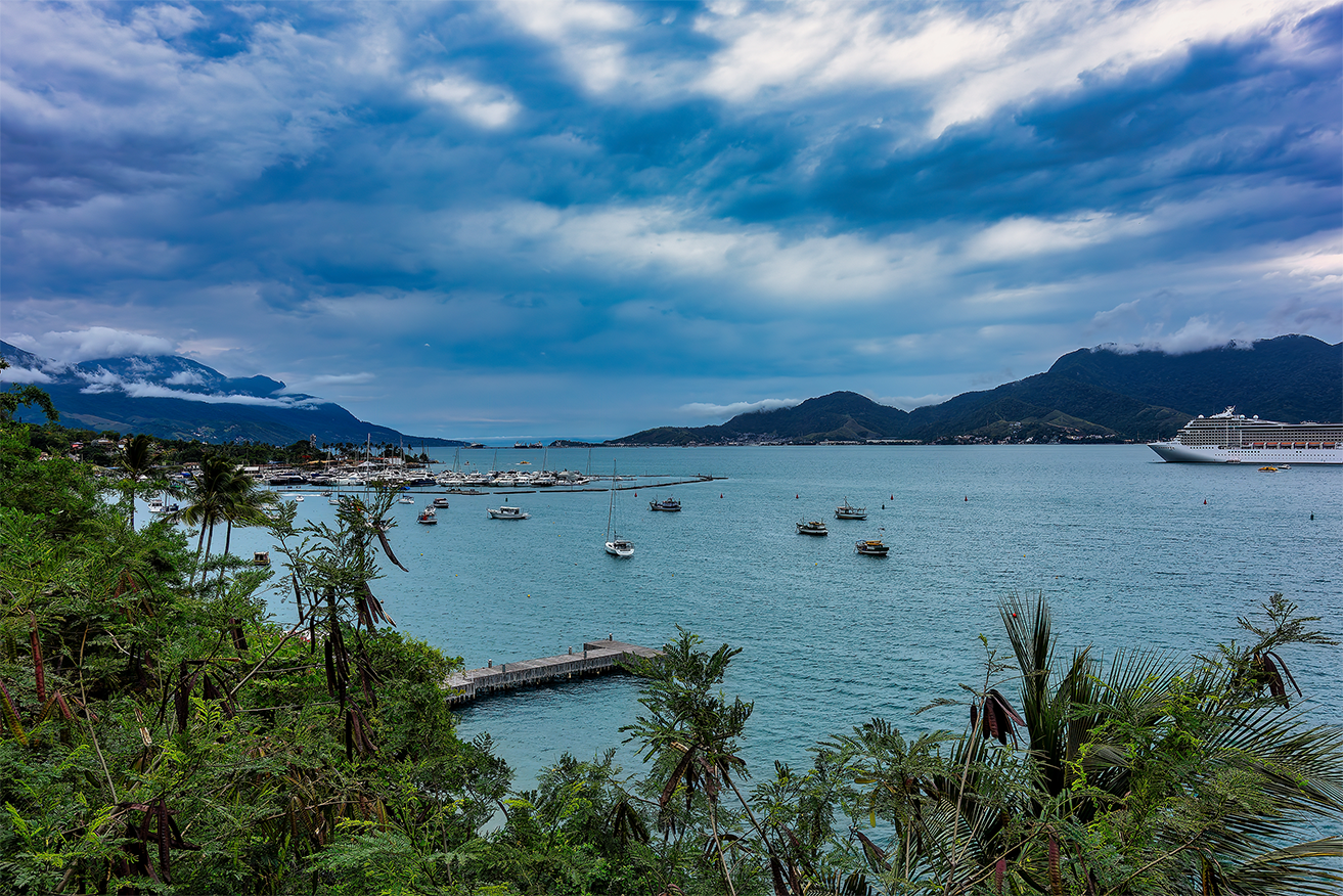 Enseada de São Sebastião cercada pela Mata Atlântica, mar calmo e vila à beira-mar. Reserve sua viagem com pontos na Livelo.