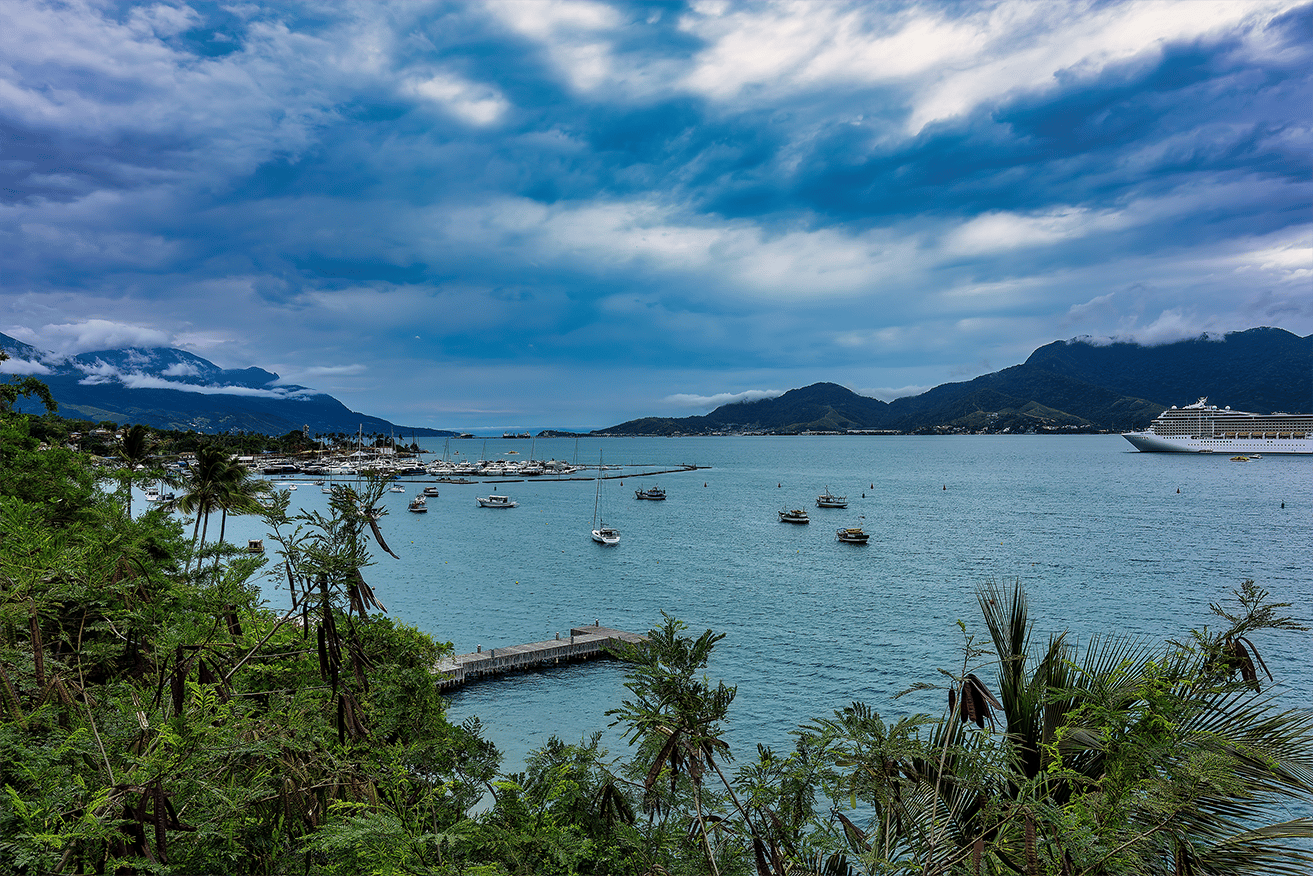Enseada de São Sebastião cercada pela Mata Atlântica, mar calmo e vila à beira-mar. Reserve sua viagem com pontos na Livelo.