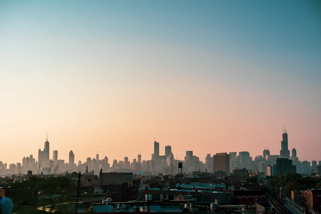 Horizonte de Chicago ao pôr do sol, com silhueta dos arranha-céus vista de longe sob céu em tons suaves. Descubra Chicago com pontos Livelo.