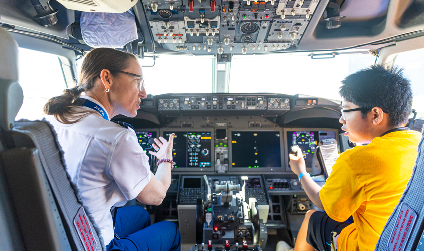 An adolescent looking in the cockpit with a pilot.