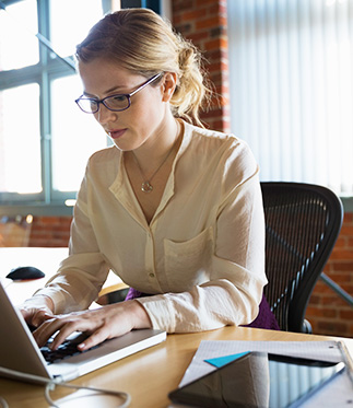 Bespectacled lady working on laptop in well-lit brick loft