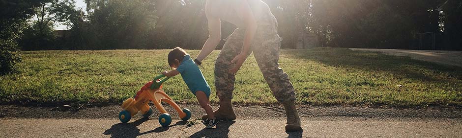 Military dad holds his child as they push a toy cart