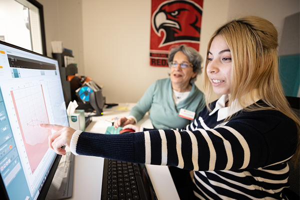 A student working on a computer while monitored by a staff member.