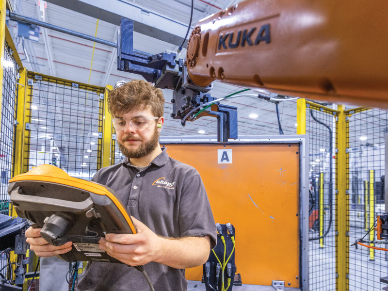 Xavier, a Work+ student using a remote to manipulate a robot at his partner Employer, Shape Corp.