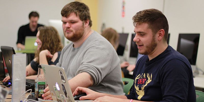 Students sit at a computer and discuss assignments.