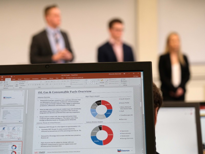 close up on a laptop showing a circle chart, with three students blurred out but standing in the background