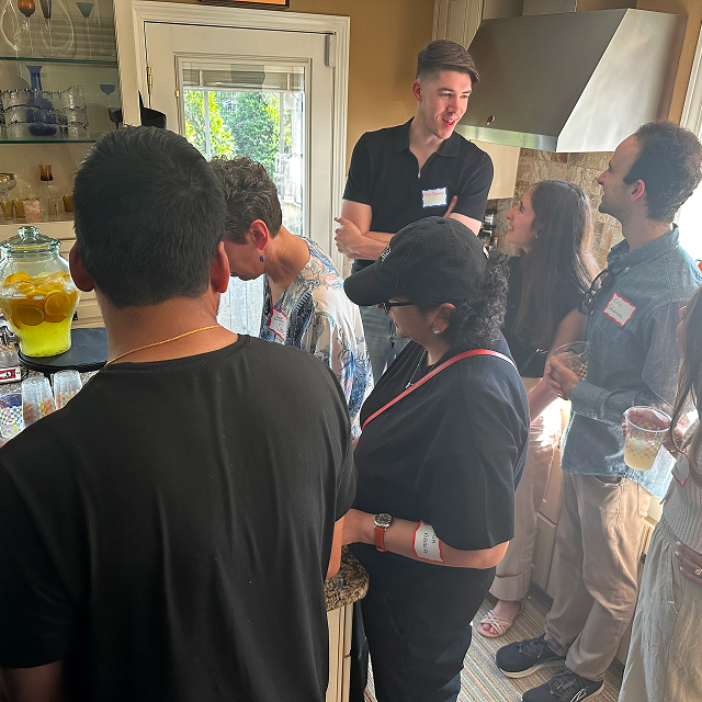 Attendees gather around a refreshment station, talking and serving drinks in a kitchen.