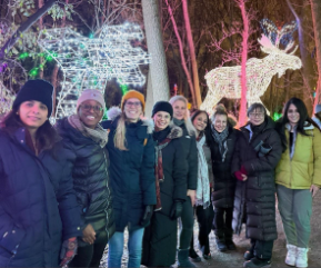 Several individuals gather for a photo, standing in front of a glowing deer display at night.
