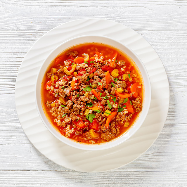 Bowl of hamburger soup with ground beef, vegetables and grains on a white plate, showcasing a hearty homemade meal.