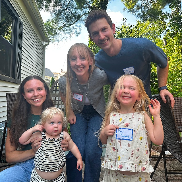 Six attendees, including two young children, pose together outdoors on a backyard patio.