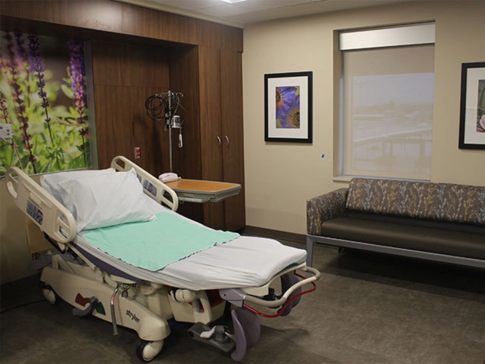 Interior of a Corewell Health birthing center room with a reclining hospital bed, couch, and wall art of flowers
