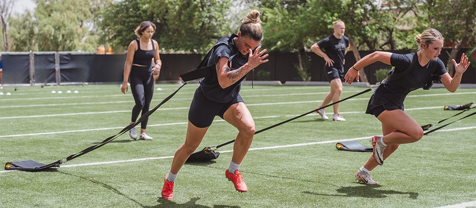 Women sprinting across a field, demonstrating strength and collaboration.