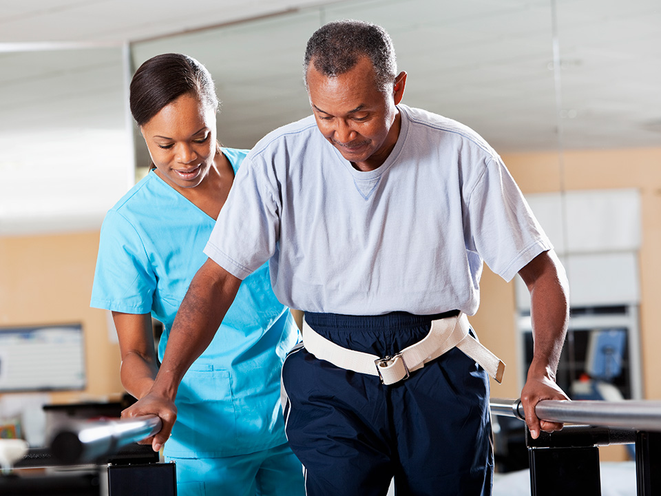 Rehabilitation specialist helps a man walk while holding onto balance bars