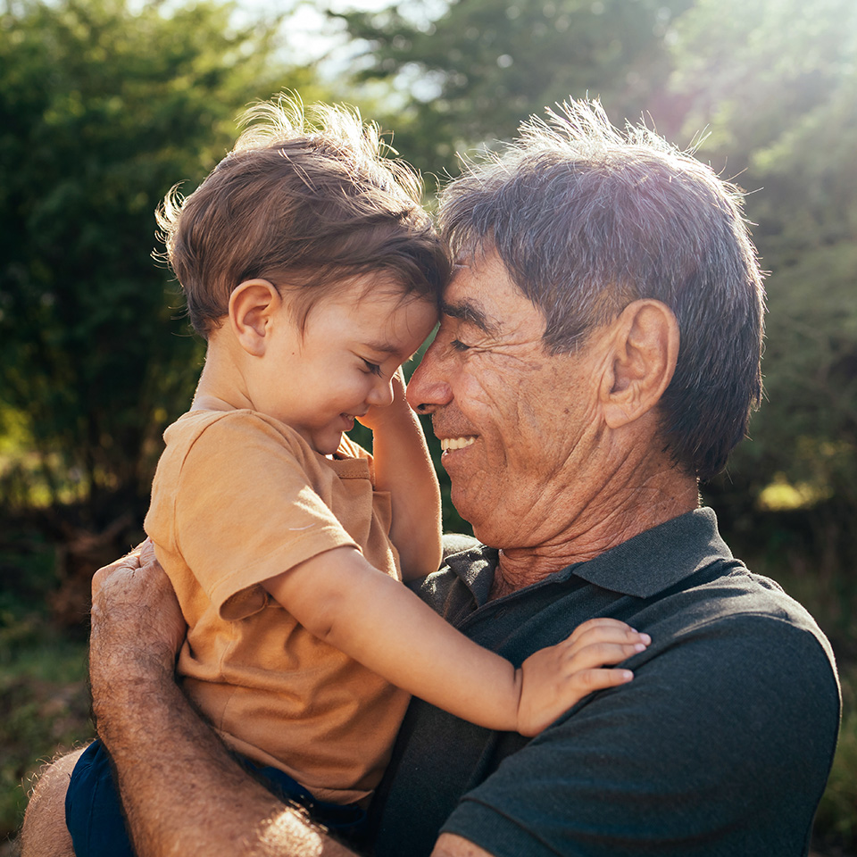 Smiling grandfather holds young grandson close to his face