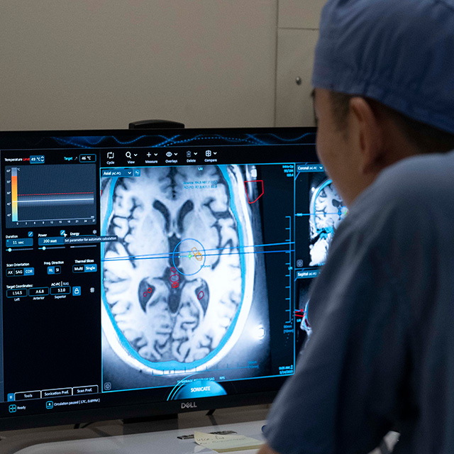A man in a hospital room intently observes a computer screen, surrounded by medical equipment.
