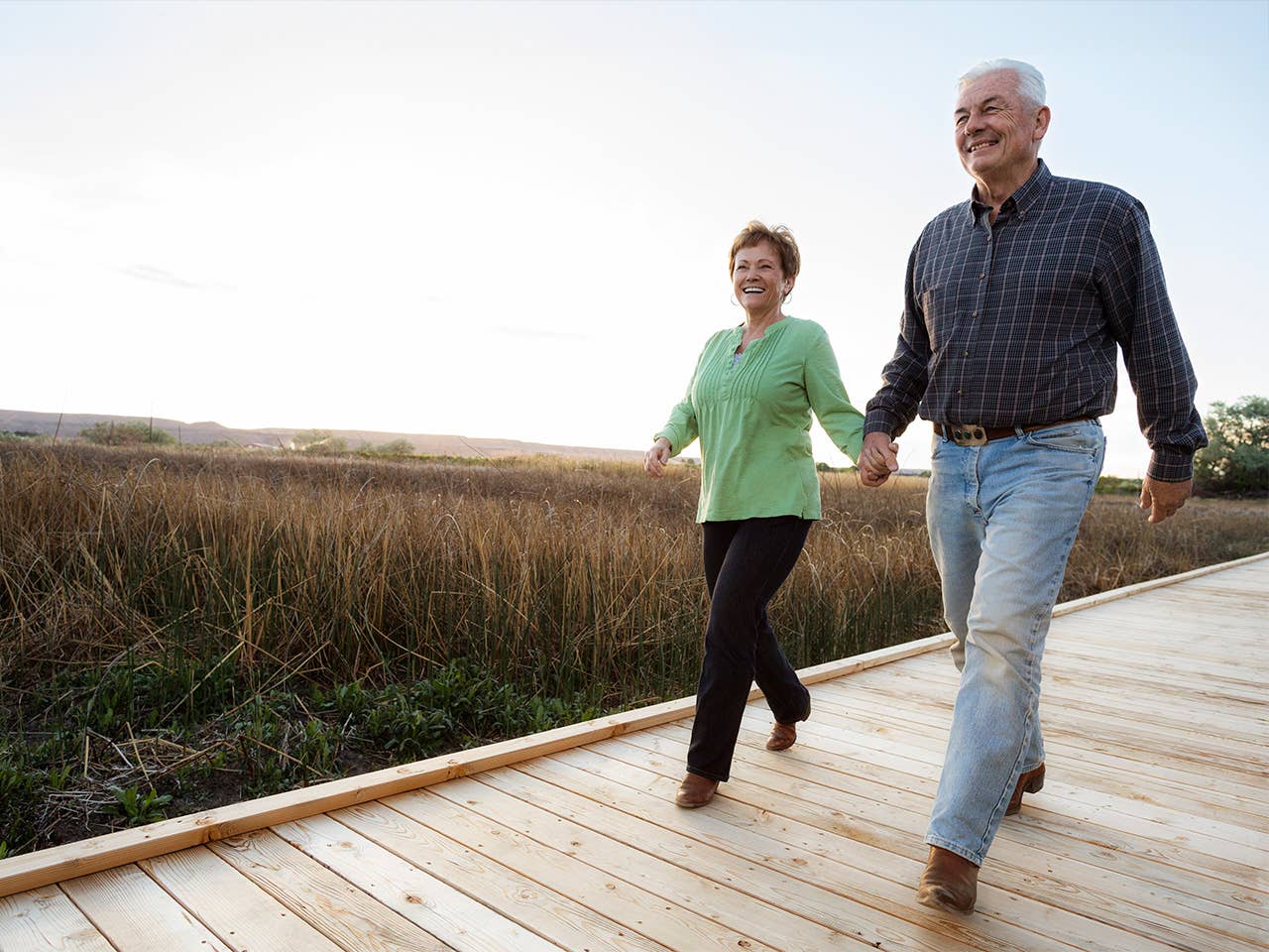 Smiling man and woman hold hands and walk along a boardwalk during a sunset