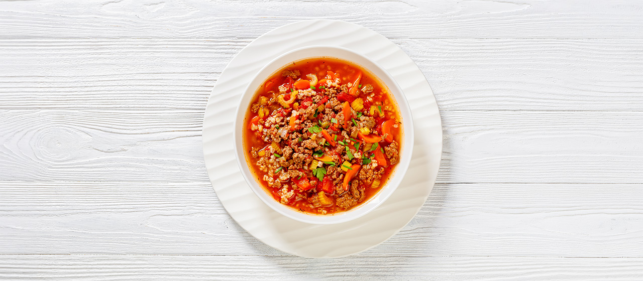 Bowl of hamburger soup with ground beef, vegetables and grains on a white plate, showcasing a hearty homemade meal.