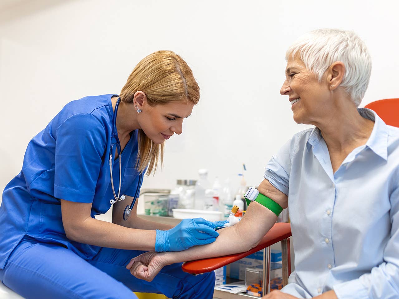 A nurse is administering a blood draw to an elderly woman in a clinical setting.