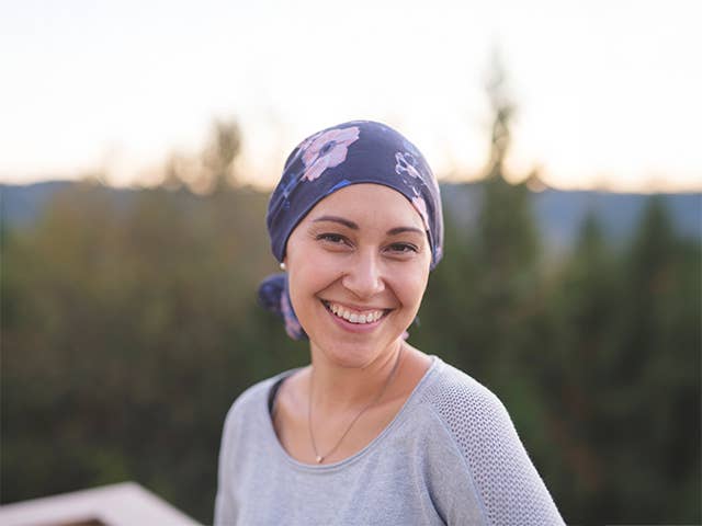 Smiling young white woman wearing a purple bandana on her head stands outdoors in the evening sunlight