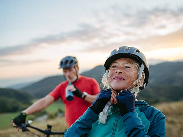 Elderly man and woman buckle bicycle helmets on their heads before starting a bicycle ride in the evening