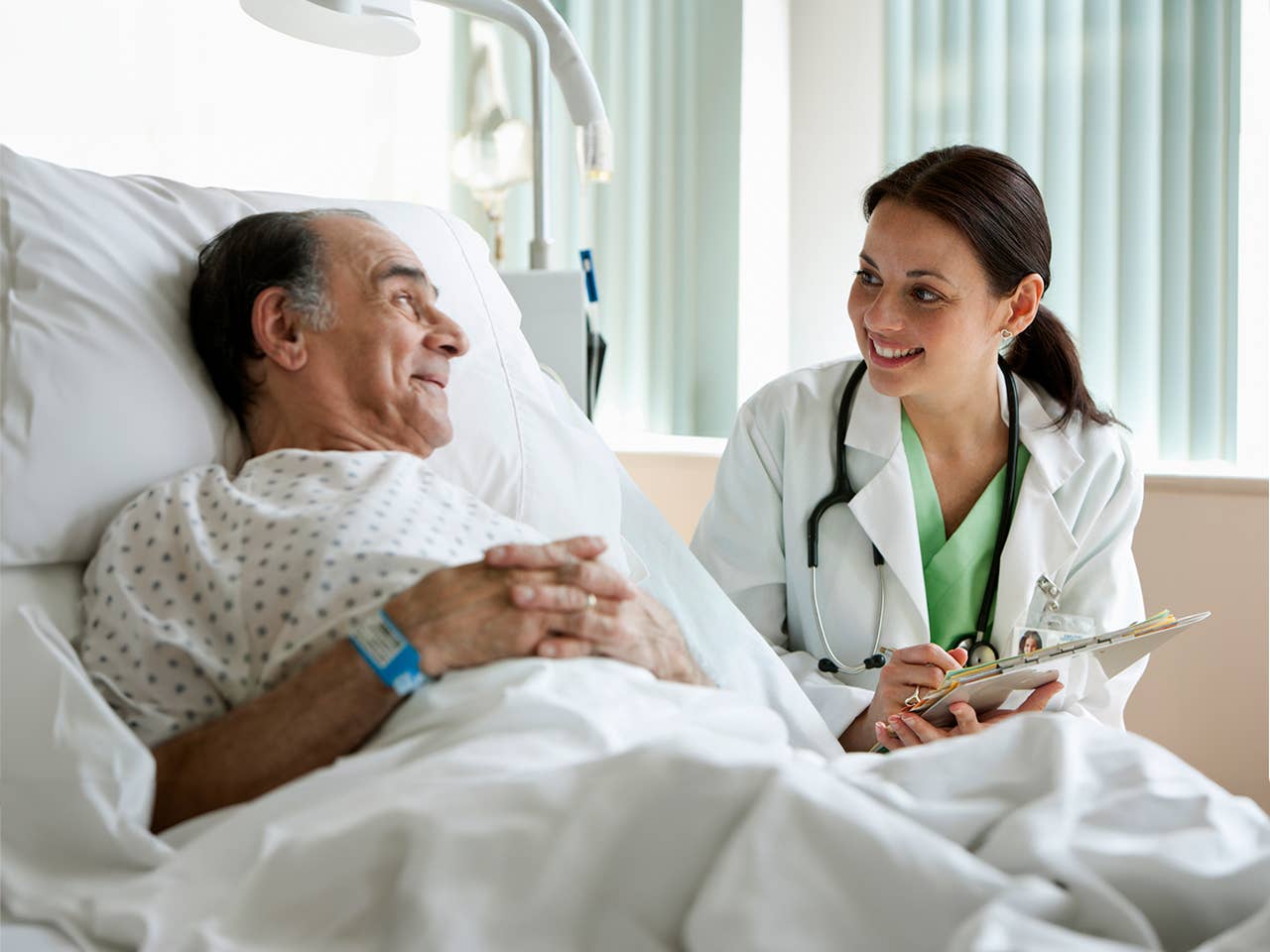 Female physician speaks with senior male patient resting in hospital bed