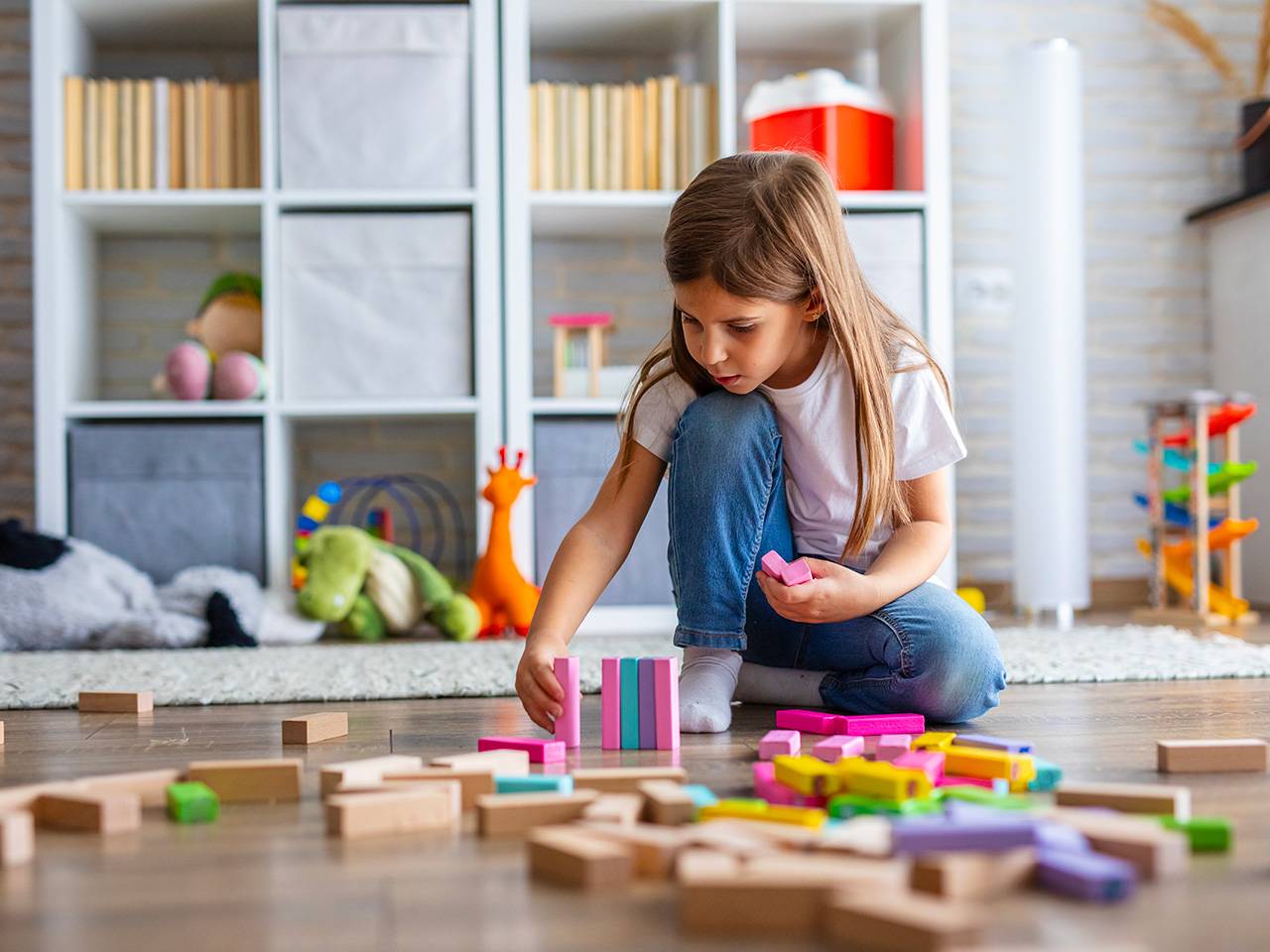 Girl wearing jeans and a white T-shirt plays with colorful blocks on a hardwood floor